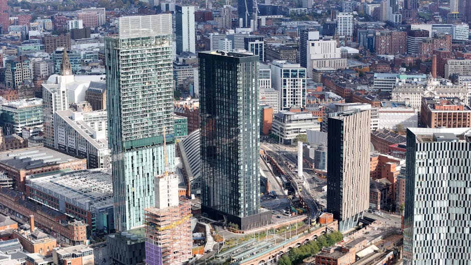 A black and white aerial view of a densely built cityscape featuring high-rise office buildings, residential apartments, and commercial structures. The scene shows a mix of modern glass and traditiona